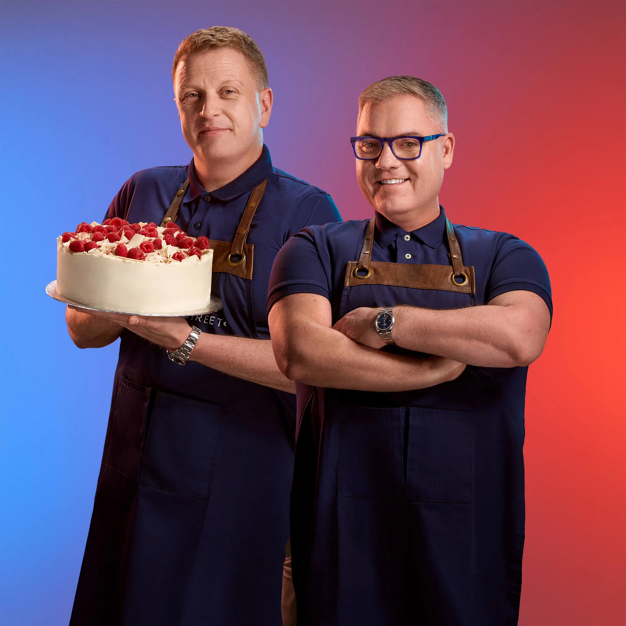 An image of two men wearing aprons and smiling on a red and blue background. One of them is holding a cake | FBD Insurance