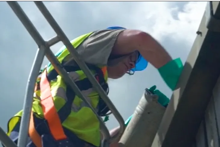 An image of a man in a hi-vis vest cleaning out the gutters on the roof of a building | FBD Insurance