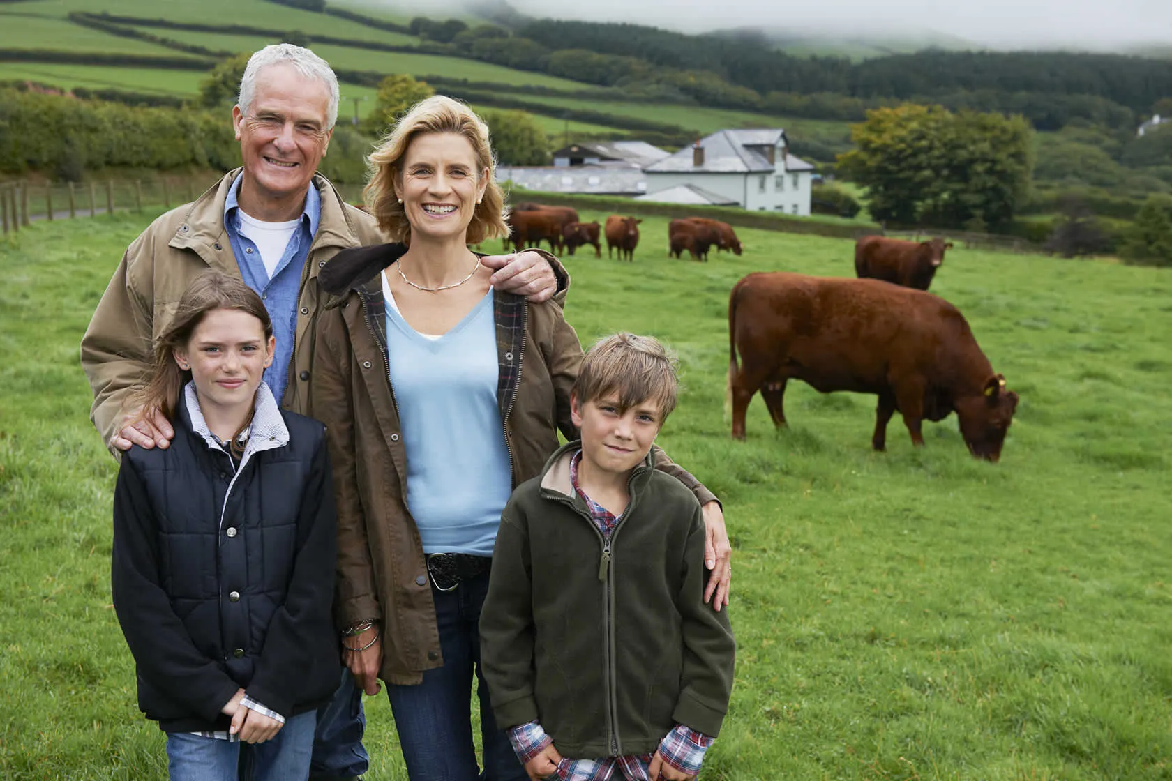 An image of a family of four (A husband, wife, daughter, and son) standing in a field of cows with a house in the background | FBD Insurance