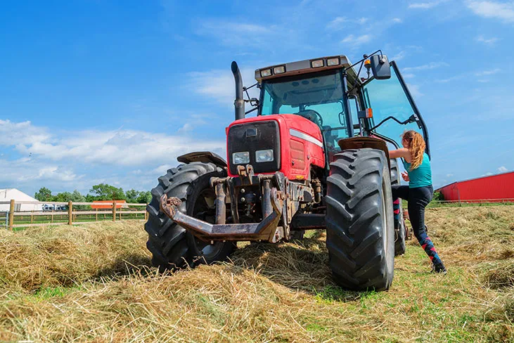 An image of a woman getting into a red tractor in a field | FBD Insurance